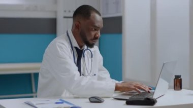 Afrika kökenli Amerikalı terapist, masa başında oturmuş dizüstü bilgisayarında hastalık uzmanlığı yazıyor.