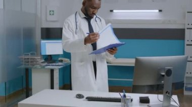 Afro-amerikan uzman doktor elinde dosya tutarak hastalık raporlarını analiz ediyor.