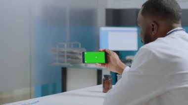 Afrikalı Amerikalı uzman doktor yeşil ekran krom anahtarlı akıllı telefonu taklit etmeye çalışıyor.