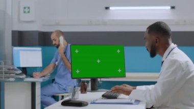 Afro-Amerikalı doktor hastane ofisinde masasında oturuyor ve sağlık hizmetlerinde çalışıyor.