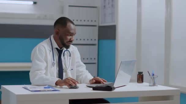 African American θεραπευτής γιατρός κάθεται στο γραφείο δακτυλογράφηση ιατρική εμπειρογνωμοσύνη, ενώ συζητάμε φαρμακευτική αγωγή — Αρχείο Βίντεο