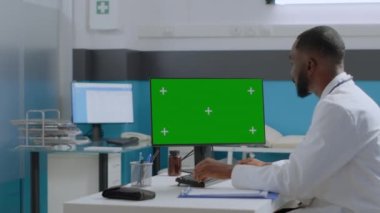 Afrikalı Amerikalı hekim doktor yeşil ekran kroma anahtar bilgisayarına bakıyor.