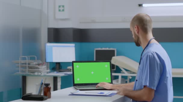 Therapist man nurse sitting at desk typing sickness expertise on mock up green screen chroma key laptop — Stock Video