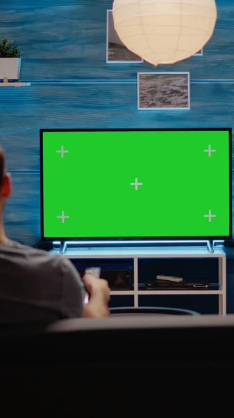 Молодой человек сидит на диване с зеленым экраном по телевизору — стоковое фото
