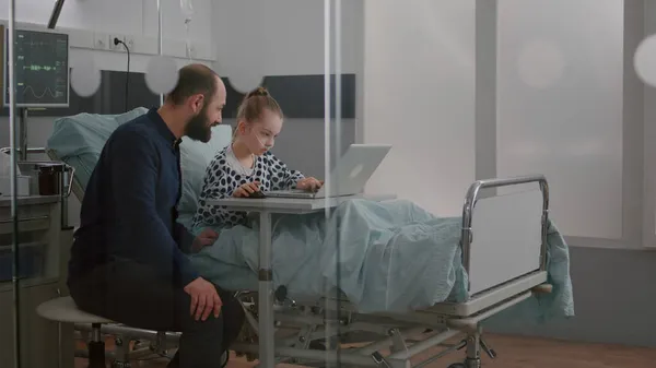 Père assis avec fille malade dans la salle d'hôpital tout en jouant à des jeux vidéo de thérapie en ligne à l'aide d'un ordinateur portable — Photo