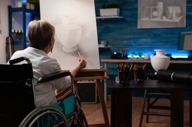 Engelli yaşlı sanatçı tuval üzerine vazo tasarımı çiziyor