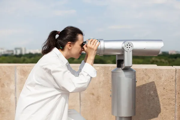 Młoda kobieta patrząca przez turystyczny teleskop lornetkowy — Zdjęcie stockowe