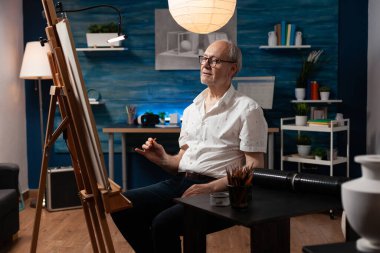 Tuval üzerine çizim yapmak için elinde kalem tutan yaşlı bir sanatçı.