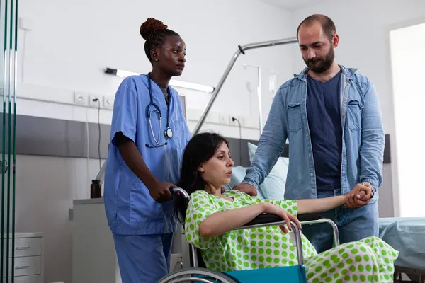 Svart sjuksköterska transporterar gravid kvinna i rullstol — Stockfoto