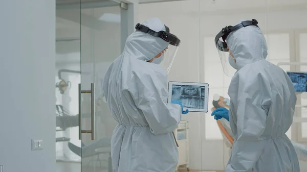 Стоматологи в костюмах ppe держат цифровой планшет с рентгеном зубов — стоковое фото
