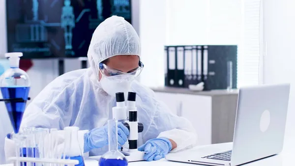 Médico pesquisador especialista vestindo equipamentos ppe olhando para o microscópio — Fotografia de Stock