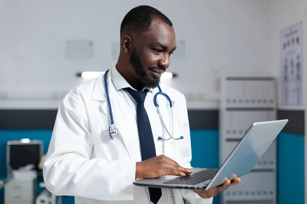 Africano terapeuta americano médico segurando laptop monitoramento de sintomas de doença — Fotografia de Stock
