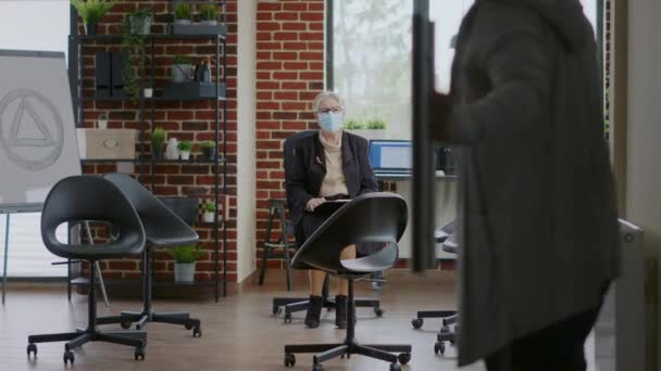 Mensen die tijdens een pandemie aankomen bij een groepsvergadering met een psycholoog — Stockvideo