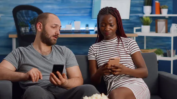 Interracial couple looking at smartphones in living room — Stock Photo, Image