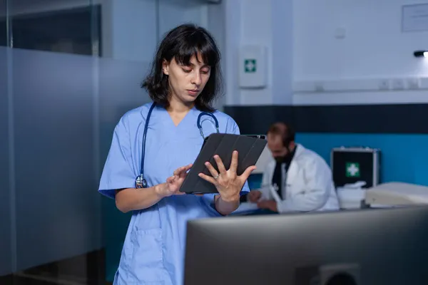 Жінка медсестра дивиться на цифровий планшет, що працює пізно вночі — стокове фото