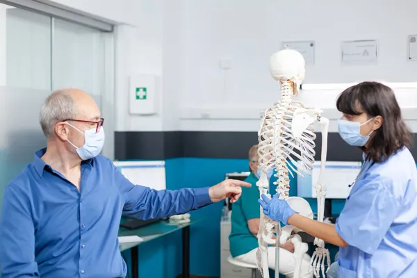 Patient et infirmière avec des masques faciaux regardant les os de la colonne vertébrale — Photo