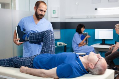 Ortopedi uzmanı bacak eklem yaralanması olan yaşlı bir hastaya yardım ediyor.