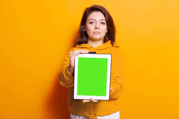 Mujer joven mostrando tableta con pantalla verde vertical en la cámara — Foto de Stock