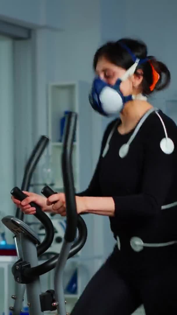 Vertical video: Doctor witing on clipboard while patient with mask running on cross trainer — Stock Video