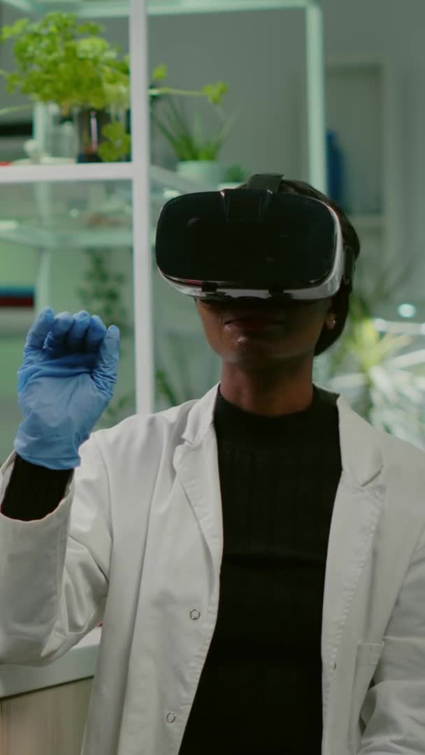 Vídeo vertical: Pesquisador biólogo africano com fone de ouvido de realidade virtual pesquisando novo experimento genético — Vídeo de Stock