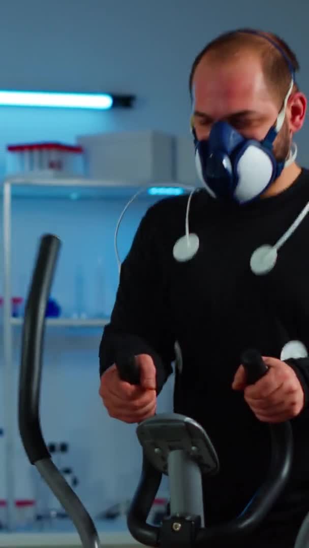 Vertical video: Athlete with mask and electrodes attached on body running on cross trainer — Stock Video