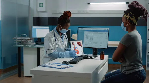 Medic con maschera viso che punta al tablet con figura del cuore — Foto Stock