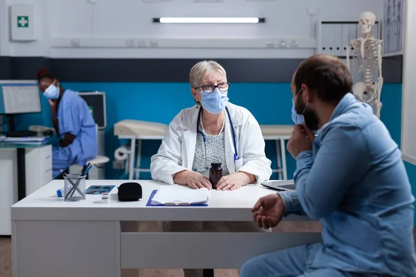 Doctor and patient with face mask talking about healthcare treatment in cabinet — Stock Photo, Image