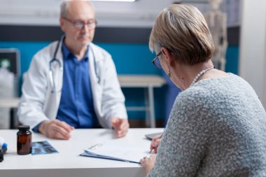 Hastalıklı yaşlı bir kadın kabinede doktorla randevu belgeleri imzalıyor.