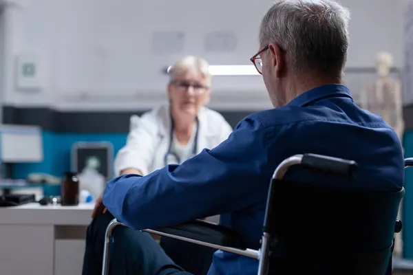 Крупним планом пацієнт сидить у інвалідному кріслі на консультації з лікарем — стокове фото