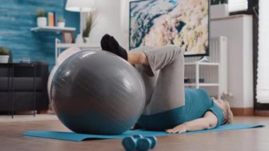 Yaşlı bir kadın spor salonunda bacaklarını esnetiyor.