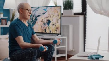 Fitness tonlama topunda oturan adam dambılları kaldırıyor