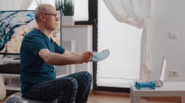 Yaşlı adam direniş bandıyla esneme egzersizi yapıyor.