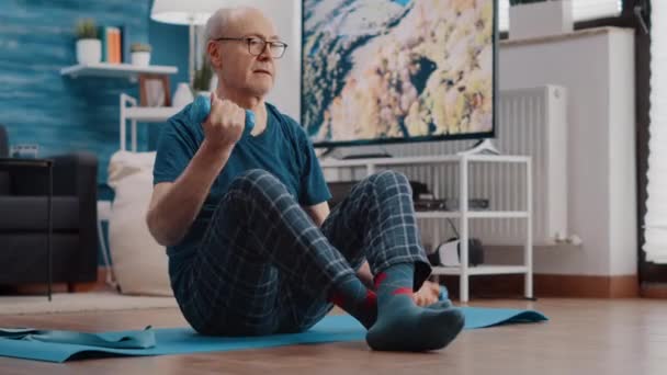 Uomo anziano che solleva i manubri per esercitare sul tappetino yoga — Video Stock