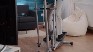 Yaşlı kişi sabit bisiklet sürüyor ve evde egzersiz yapıyor.
