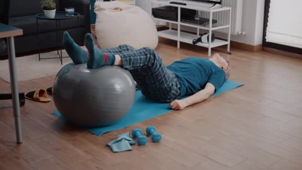 Leeftijd persoon met behulp van toning bal te rekken benen spieren op yoga mat — Stockvideo