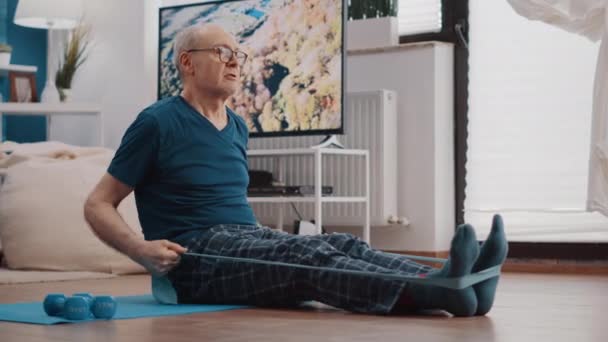 Hombre anciano usando banda de resistencia para estirar brazos y piernas — Vídeos de Stock