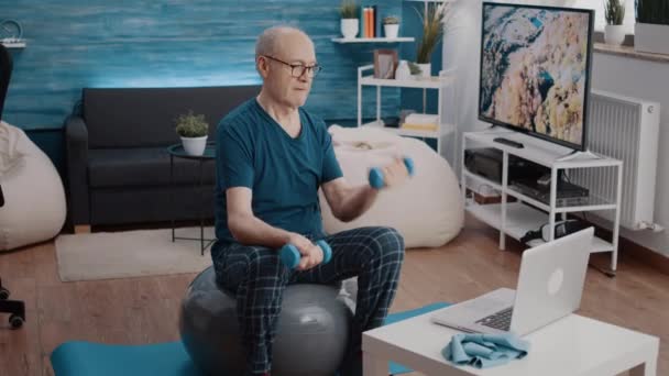 シニア男座っているトーニングボールと使用ダンベル — ストック動画