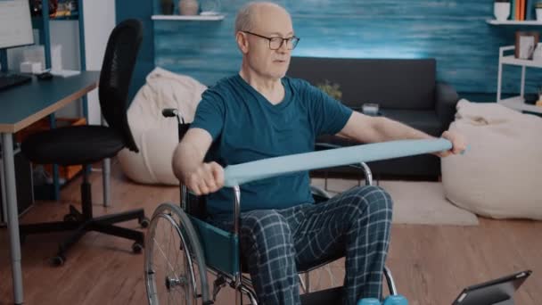 Mężczyzna siedzi na wózku inwalidzkim i ćwiczy z taśmą oporową — Wideo stockowe