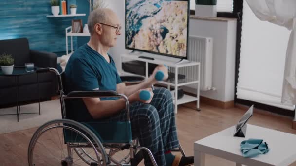 Gepensioneerde zit in een rolstoel en doet oefeningen met halters — Stockvideo