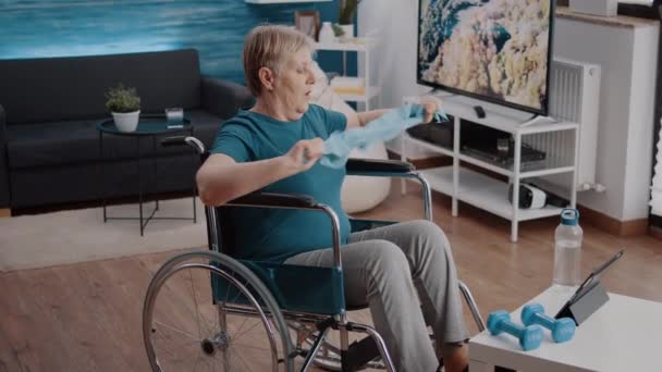 Person sitzt im Rollstuhl und zieht Widerstandsband zum Dehnen — Stockvideo