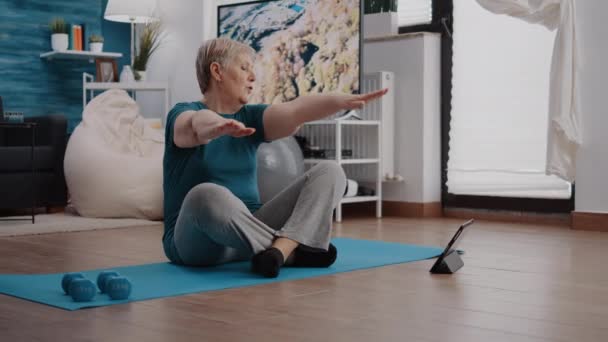 Oudere volwassene doet fysieke oefening en kijkt video op tablet — Stockvideo