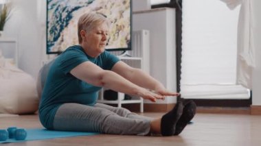 Yaşlı kadın yoga minderinde esneme egzersizi yapıyor.