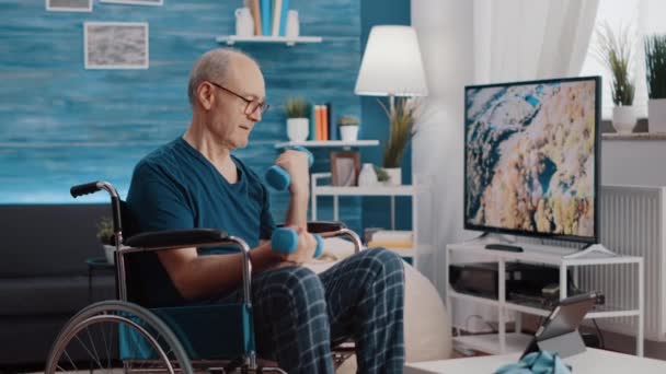 Emeryt siedzący na wózku inwalidzkim i podnoszący hantle — Wideo stockowe