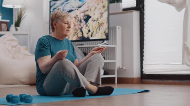 Ältere Person sitzt in Lotusposition auf Yogamatte, um zu meditieren — Stockvideo