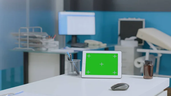 Falsificare computer tablet schermo verde con display isolato in piedi sul tavolo in ufficio ospedale vuoto — Foto Stock