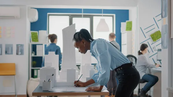 Afrikaanse Amerikaanse architect analyseert blauwdrukken plan en bouwmodel om project structuur te creëren — Stockfoto
