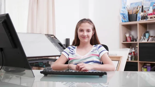 Portret uśmiechniętego dziecka patrzącego w kamerę siedząc przy biurku — Zdjęcie stockowe