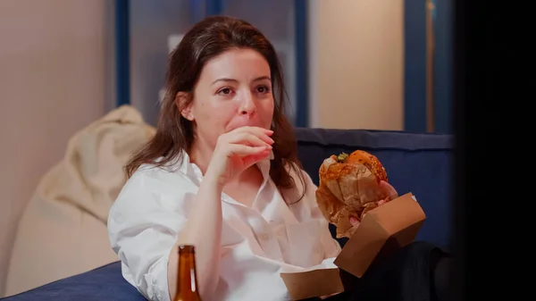 Obchodní žena sleduje televizi jíst burger v obývacím pokoji — Stock fotografie