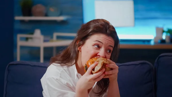 거실에서 햄버거를 먹고 있는 백인 여성 — 스톡 사진