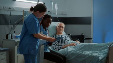 Afrikalı Amerikalı doktor hasta hastayla yatakta konuşuyor.